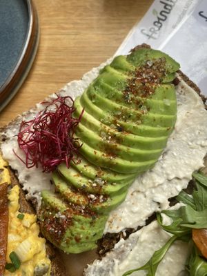 Slice of multigrain seed bread with white bean feta spread, avocado and beetroot sprouts  at Froindlichst in Berlin