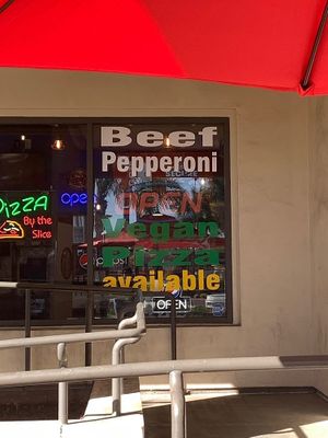 Signage on restaurant window promoting vegan pizza at University Pizza Company in Riverside