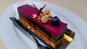 This vegan cake has four layers. At the bottom a crunchy nougat, then cake, then chocolate mouse, and finally a layer of gelled berries. It is topped with some nuts, a black berry  at Zenhäusern in Sierre