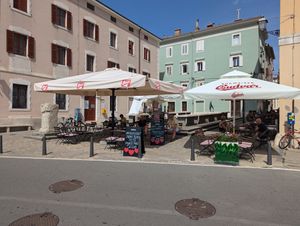Outdoor seating with sign mentioning vegan pizzas at Caffe Galeria in Piran
