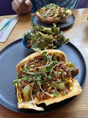 Brunch dog with mung bean scrambled “eggs”, salsa verde with avocado, tofu bacon, potato crisps, cucumber pickles, greens, tofu hollandaise with a side “no parm no foul” sa at Good Dogs Plant Foods in Vancouver