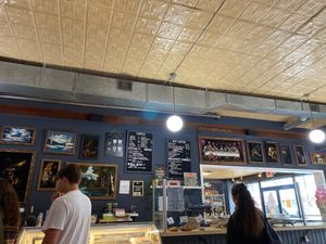 Counter with menu (showing vegan breakfast sandwich and plant milk beverage options) and pastry case (including vegan pastries) at Crumb Bum in Littleton