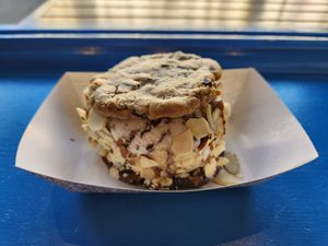 Cookie sandwich with one vegan chocolate chip cookie and one vegan fudge brownie cookie, vegan chocolate chip ice cream topped with almonds. Chocolate chip cookie side at The Baked Bear in San Francisco