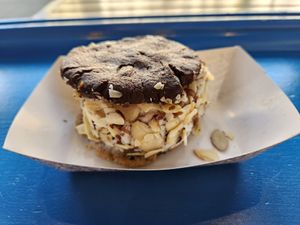 Cookie sandwich with one vegan chocolate chip cookie and one vegan fudge brownie cookie, vegan chocolate chip ice cream topped with almonds. Fudgy brownie cookie side at The Baked Bear in San Francisco
