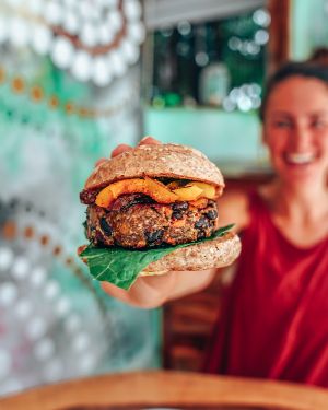 BLISS BEAN BURGER - Our house veggie burger made w/ beans, carrots, oats + coconut served on a wild fermented bun. Topped w/ sundried tomatoes, cured eggplant, coconut bacon, pesto at Naked Foods in Nosara
