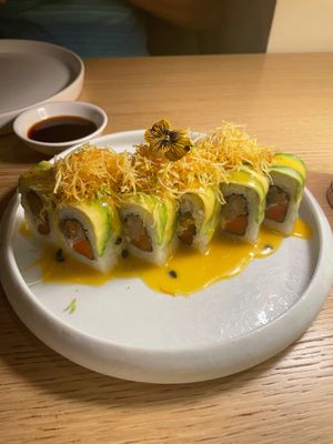 Uramaki Dragon roll - Breaded oyster mushroom, cashew cheese and carrot. Topped with avocado, passion fruit sauce and potato strings. at MUDRA Plant Based  in Madrid