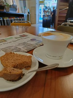 An oat cappuccino, vegan banana bread, and a newspaper on the big table. at De Koffiesalon Centrum in Amsterdam