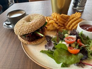 Falafel in a sesame bagel with hummus and vegan tatziki. Oat milk flat white in the back  at WASBAR in Bruges