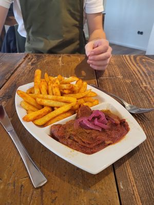 Scharf gegrillte Seitancurrywurst in
selbstgemachter Curry-Tomatensoße,
serviert mit pink-gepickelten Zwiebeln
und einer Portion Pommes at Weltkind in Werneck