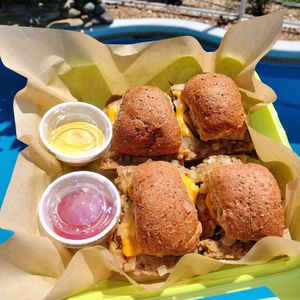 BELLIE BOMBS our spin on our favorite takeout sliders. Grilled then steamed with onions topped with American cheese and a pickle on a sprouted whole grain bun served with a side of at Garden of Feeding  in West Melbourne
