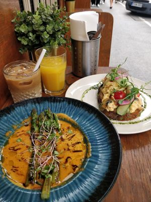 Iced oat latte, fresh orange juice, creamy bell pepper soup, and scrambled eggs with added mushrooms on sourdough toast. at Garzon Café  in Budapest