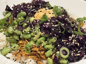 Eine bunte Korean Style Bowl mit weißem Reis, Edamame, Rotkohl, knusprigem Gemüse, Frühlingszwiebeln, Sesam und einer cremigen Sauce in der Mitte  at Ti's Café in Minheim