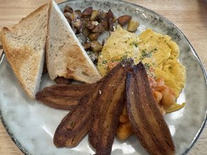 Deftiges Frühstück mit Kichererbsen-Omelett, Bratkartoffeln, gebackenen weißen Bohnen in Tomatensoße, knusprigem veganem Bacon und getoastetem Brot.  at Ti's Café in Minheim