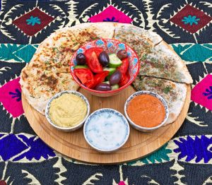 Qutab set.
Two stuffed Qutab flatbreads: 1 with greens, 1 with potato & vegan cheese, topped with sumac & greens, served with fresh salad and three sauces: hummus, chaka yoghurt,  at Dervish in Berlin