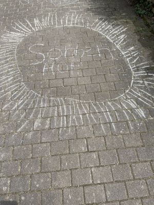 Chalk drawing on the ground: a big sun and the word „Sonnenhof“ inside  at Sonnenhof Hohenfelden in Hohenfelden