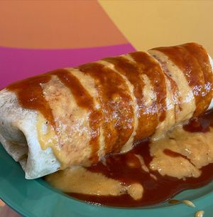 Bomb Burrito filled with taco meat, black bean and corn salsa, cilantro lime rice, pico de gallo, and Baja ranch, topped with enchilada sauce and nacho cheese at devil's lettuce in Richmond