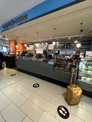 Exterior and has communal seating plus small tables and chairs  at LCY - Caffe Nero in East London