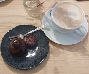 A chocolate brownie with chocolate mousse with chocolate on top, a blueberry macaron and a hot chocolate. at ima vegan  in Hamburg