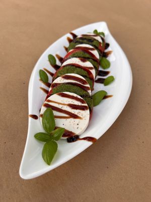 Caprese Salad. An Italian Classic with a Vegan Twist. In-House Made Cashew "Mozzarella" paired with fresh pesto, sliced tomato and fresh basil. Ask for a Truffle twist and enjoy. at Pacha Roots in Miami