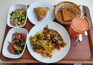 Two salads on the left, one pumpkin somsa and some flatbread on top, two veggie mains on the large plate, and fresh carrot juice. at Do'stlar in Tashkent