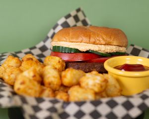 Chipotle Black Bean Vegan Burger served on our fresh baked vegan bun.  Topped with Tomato, Cucumber and Sriracha Cashew Cream.  Served with Tots - also vegan. at The Atom Bistro and Coffee Bar in Glide