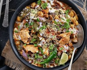 Hot Samosa Chaat is a popular Indian street food made with crispy fried samosas, mashed and topped with chutney, yogurt, and spices, and sometimes garnished with lentil sticks and chopped onions. at Jagdish Farshan in Irving