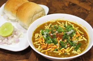 Sev Usal is a spicy and flavorful Gujarati street food dish made with boiled and mashed beans, topped with sev, onions, chutney, and served with bread (pav). at Jagdish Farshan in Irving