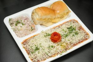Cheese Pav Bhaji consists of a spicy vegetable curry (bhaji) served with a soft bread roll (pav), topped with a generous amount of grated cheese at Jagdish Farshan in Irving