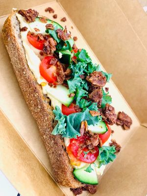Multigrain bread, hummus (tahini, chickpeas, salt, lemon juice, garlic), coconut “bacon” crumbles, cucumber, tomatoes, lemon, kale, smoked citrus sea salt. Photo by Veg Lakesho at Good Judy's Market & Juice Bar in Grand Rapids