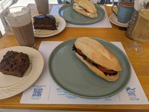 Fatia de bolo de banana com gotas de chocolate, pão de melado, sanduíche de tempe, macchiato de doce de leite, vitamina protéica, sanduíche de tofu minas e capuccino at Casa Madal in Sao Paulo