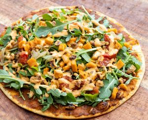 Aleppo FLAT: Spicy red pepper, chickpea and walnut spread layered on thin lavash bread and topped with arugula, roasted tomato, sautéed onion, sweet potato, & walnuts and dressing at worldFLATS - Montclair in Montclair