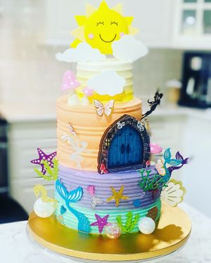 3 tier birthday cake. Each layer featuring a fantasy version of the Earth. The ocean with mermaids, land with fairies and the sky with a smiling sun.  at Austin Kind Cakes in Austin
