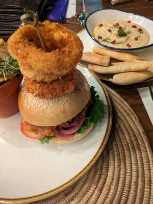 Vegan burger with onion rings and hummus and flatbread in the back at The Village Garden in Windhoek