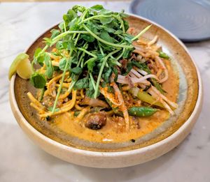 Shiitake Peanut Laksa: red chilli coconut broth, stir fried shiitake tender stem broccoli, noodles, chilli oil, crushed peanuts, fragrant herbs at Mildreds - Victoria in South West London