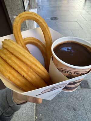 A to-go container holding churros and a cup of chocolatee  at Tacita De Plata in Madrid