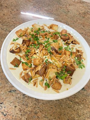Yalanji Fatteh: a layered dish featuring grape leaves, rice, onions, vegetables, and pomegranate molasses, topped with a nut-based yogurt & Tahini sauce and roasted nuts. at Zada Kitchen in Ramallah