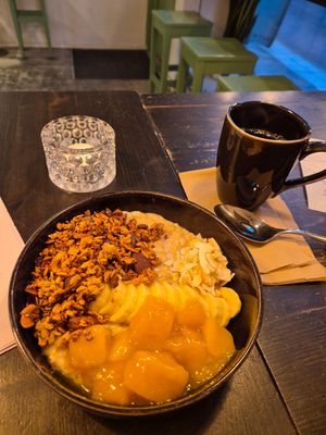 Porrige with mango compott, coconut, granola and banana. Served with hot foamed  oat milk. at Grain Café in Stockholm