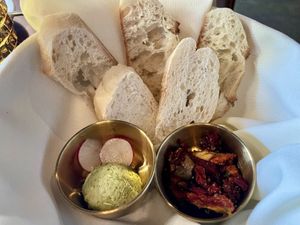 Small bread service with an herb butter, radishes, and cracked pepper. Those are sun-dried tomatoes in the container on the right.  at Marian Cocktails and Kitchen in Raleigh