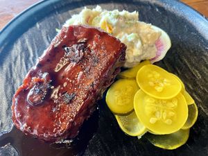 Whiskey and cola rib plate with Mimi’s potato salad, squash, and Vidalia, pickles and radish. The sauce is a house made whiskey and cola black pepper barbecue sauce.  at Marian Cocktails and Kitchen in Raleigh