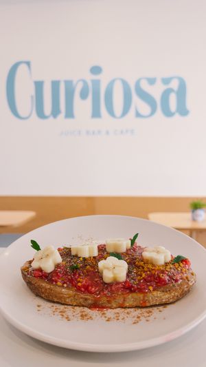 100% Vegan: Creamy almond butter, fresh raspberry and chia compote, sprinkled with bee pollen and cinnamon, topped with banana slices, on toasted sourdough bread. at Curiosa | Cafe & Juice Bar in Mexico City