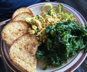 Breakfast scramble served w/ garlic-steamed greens & brown rice toast, seasoned tofu, green peppers, onions, mushrooms, broccoli, & carrots. Vegan cheese blended into seasoned tofu, scrambled w/green peppers onions, & mushrooms topped w/tomatoes. at The Wayward Vegan in Seattle