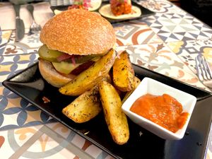 Hamburguesa casera de soja y remolacha con "cheddar", encurtidos
y mayo siracha en pan de semillas con patatas asadas y salsa BBQ  at VEGA - Luna in Madrid