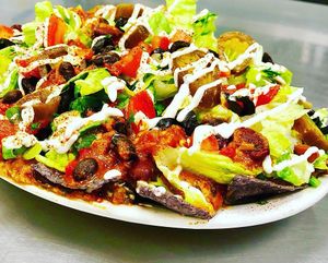 Fully Loaded Vegan Nachos.  Organic corn chips smothered with vegan chili con queso, topped with romaine, tomato, black olive, green onion, cilantro, jalapeño, cashew sour cream and chili spice. YUM1 at Juice Junkies in Keller