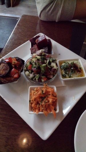 1st course of lunch menu - a plate of salads for two consisting of tomatoes, cucumber, red onion and parsley; delicious carrots with nuts; cooked beet with marinade; green tahini sauce; roasted eggplant with red peppers at Hummus in Barcelona