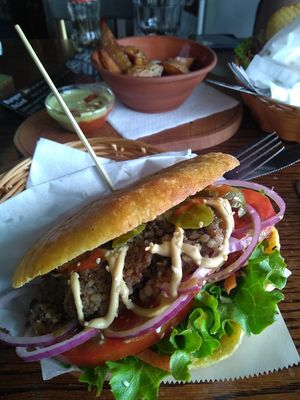 "Public" burger with corn bun (pickles, salad, sauces) and wedges at Public Bar & Vegan Kitchen in Bled