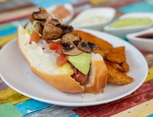 Dogo callejero: vegan hot dog wrapped in vegan ham, with potato cheese, soy-bacon bits, onion and tomato, guacamole and grilled mushrooms with a side of fine seasoned potato wedges at Vegan House in Culiacan