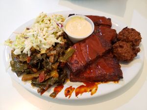 Large combo plate with smoked seitan short ribs and smoked tempeh with BBQ sauce, collard greens, creamy coleslaw, and hush puppies with lemon remoulade. Photo taken May 2019. at Homegrown Smoker in Portland
