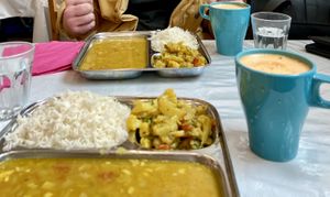 Two metal trays with dahl, rice and vegetables. Juice in two cups  at Thenga Cafe in London