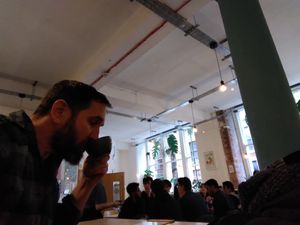A bearded man sips in front of big windows. at Idle Hands in Manchester