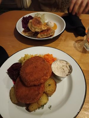 Front: celeriac schnitzel and dill potatoes with sides of beets, cabbage, and carrot slaw, plus a cup of horse radish. Back: pierogies and mustard with colorful cabbage sides. at Apteka in Pittsburgh
